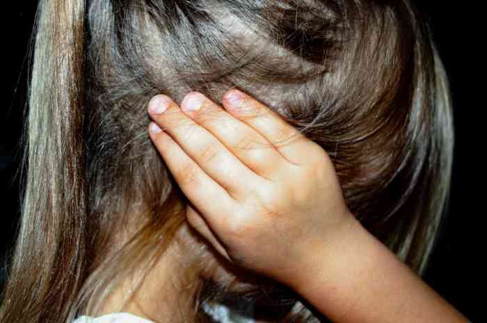 Profile of a child in pain holding her head inside her hands