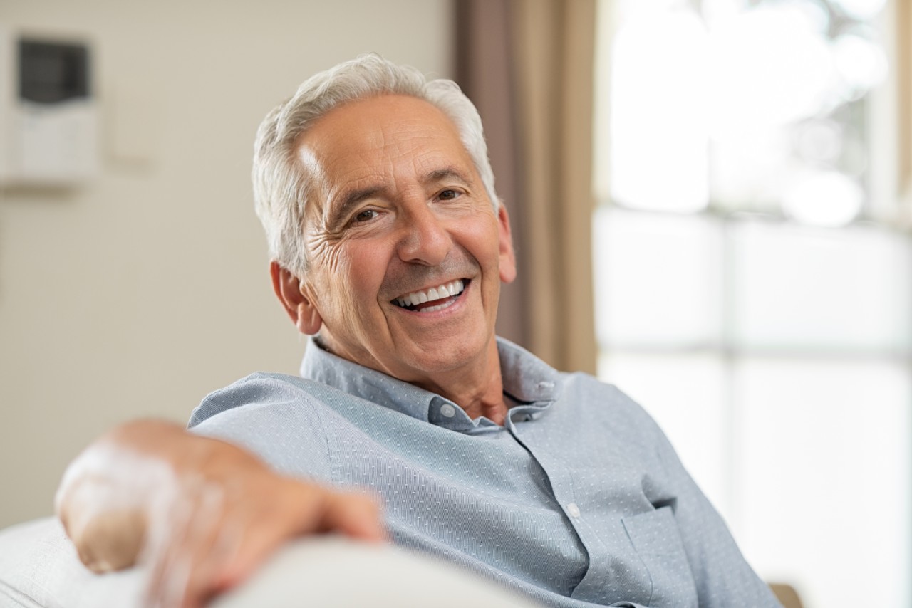 Elderly man smiling, sitting on a sofa