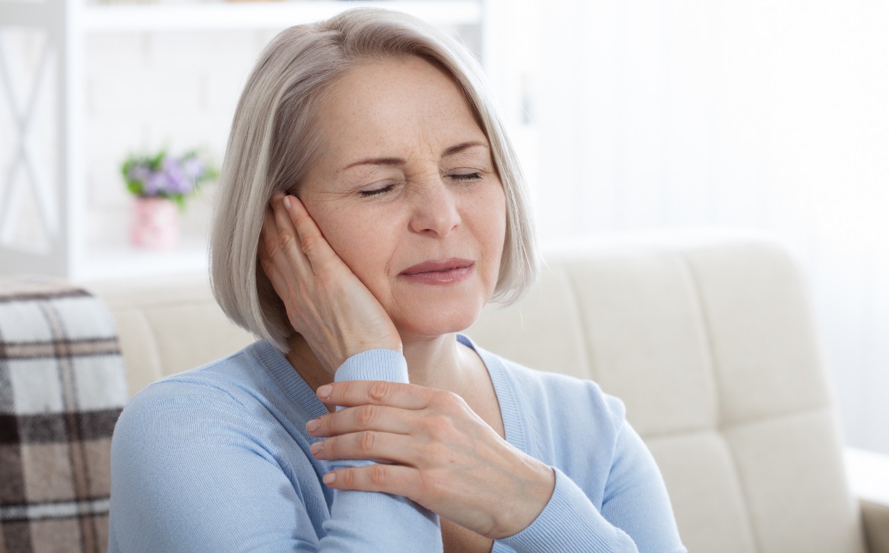 Elderly woman in pain holding her ear on a sofa