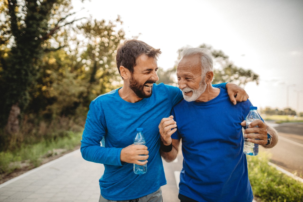 An old man with a younger generation smiling at each other while exercising outside