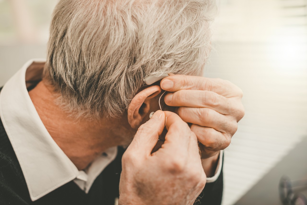 A man from behind inserting a hearing aid in his ear
