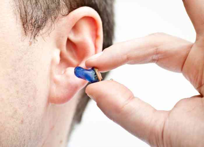 A close up of a man holding an invisible hearing aid close to his ear