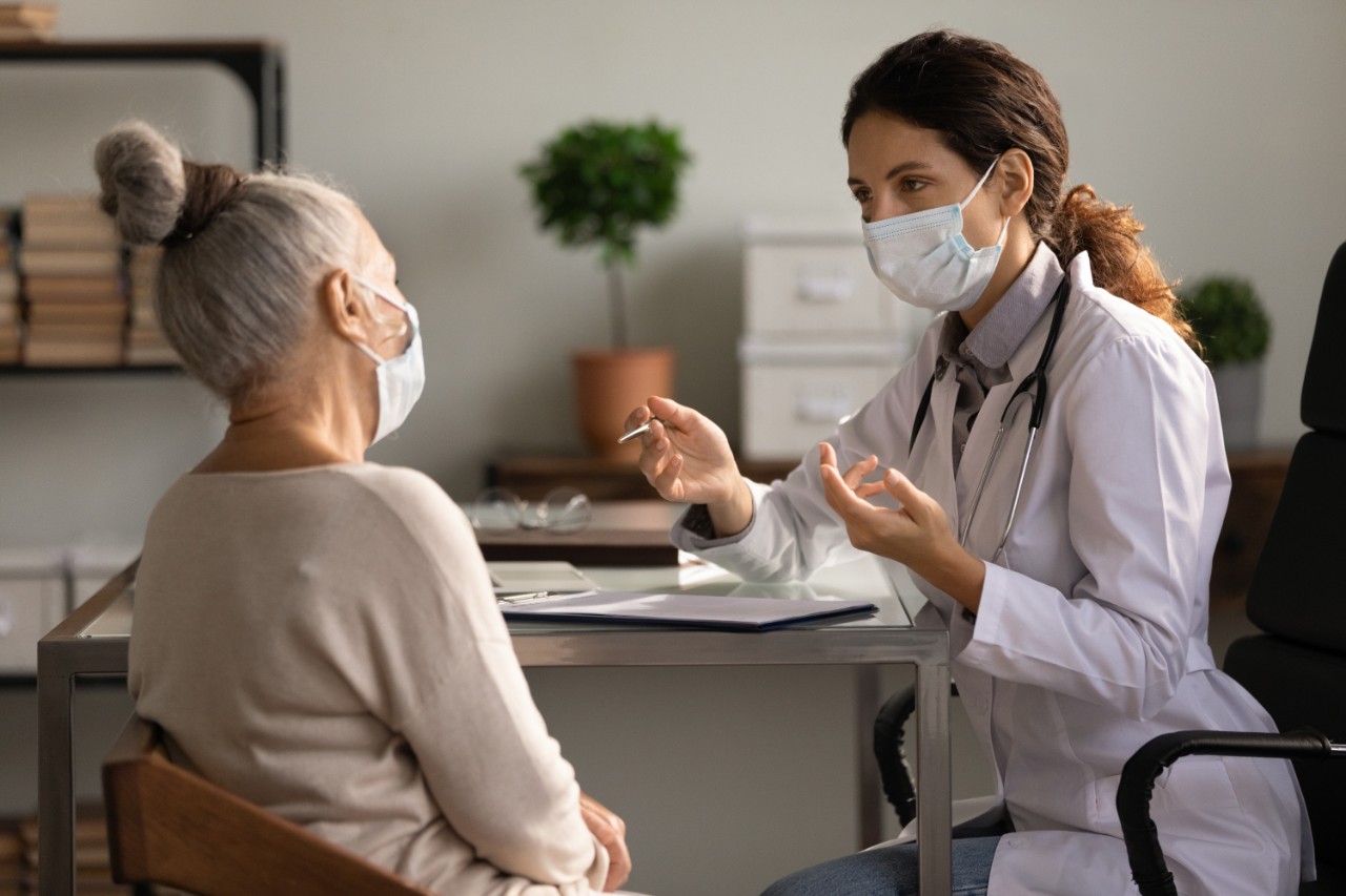 an audioprothesist helping a woman putting the hearing aid while wearing a face mask