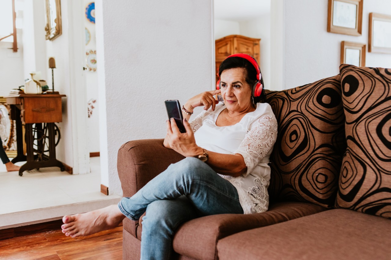 A woman sitting on the couch looking at her phone with headphones on