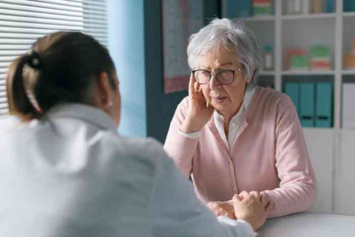Eine ältere Frau erklärt der Ärztin ihre Ohrenschmerzen