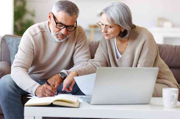 Un vieil homme et une femme regardant leur ordinateur portable, assis dans leur cuisine 