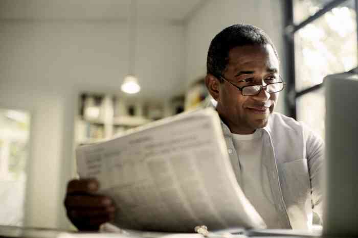 Person reading news on laptop and newspaper