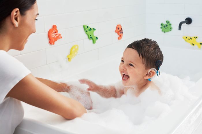 Mother giving a bath to a child with hearing aid