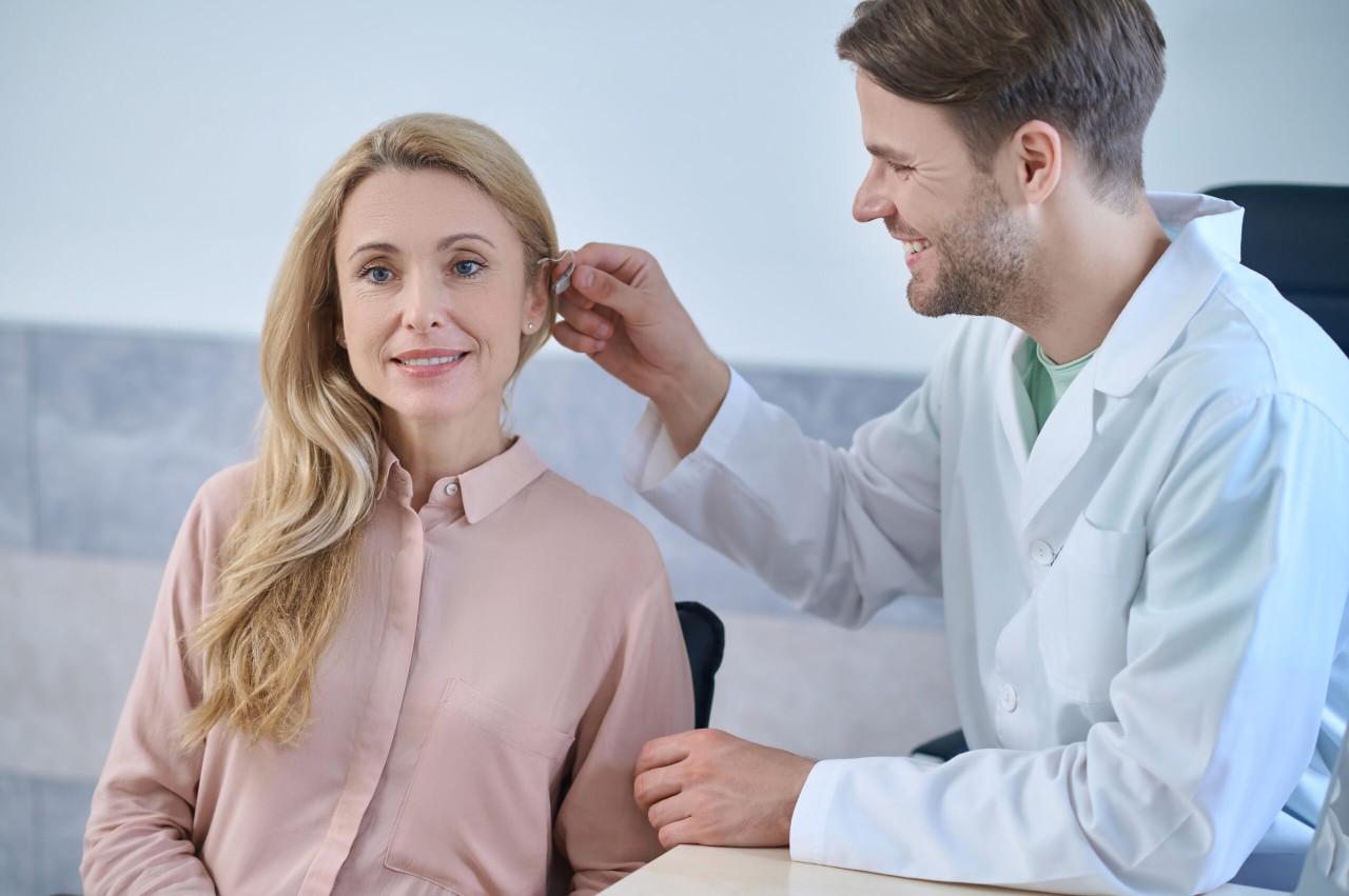 Un médecin essayant un appareil auditif sur une patient