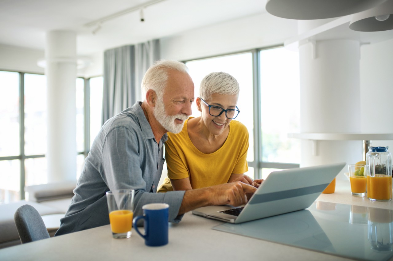 An old man and woman looking at their laptop, sitting in their kitchen