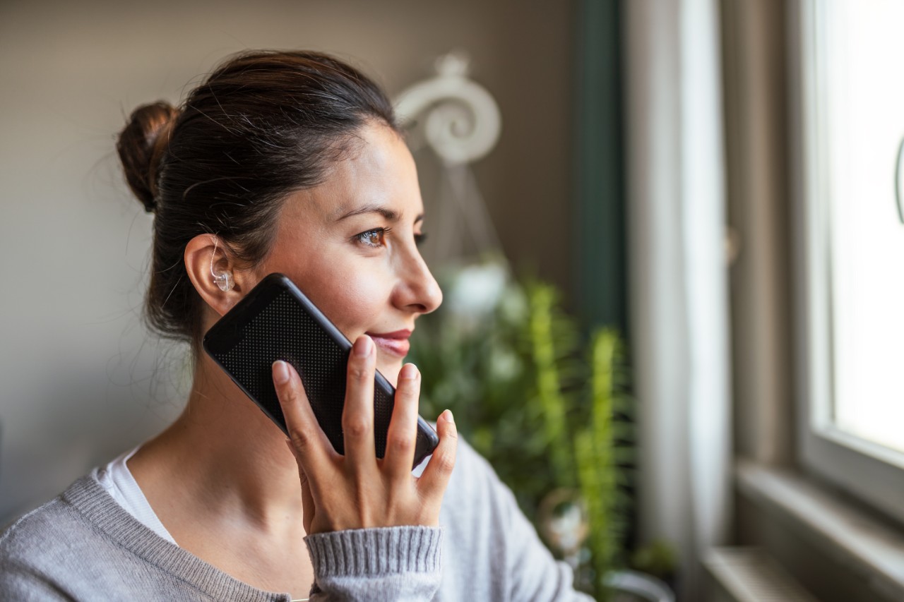 Giovane donna tiene il suo telefono, risponde a una chiamata mentre usa un apparecchio acustico per acufeni