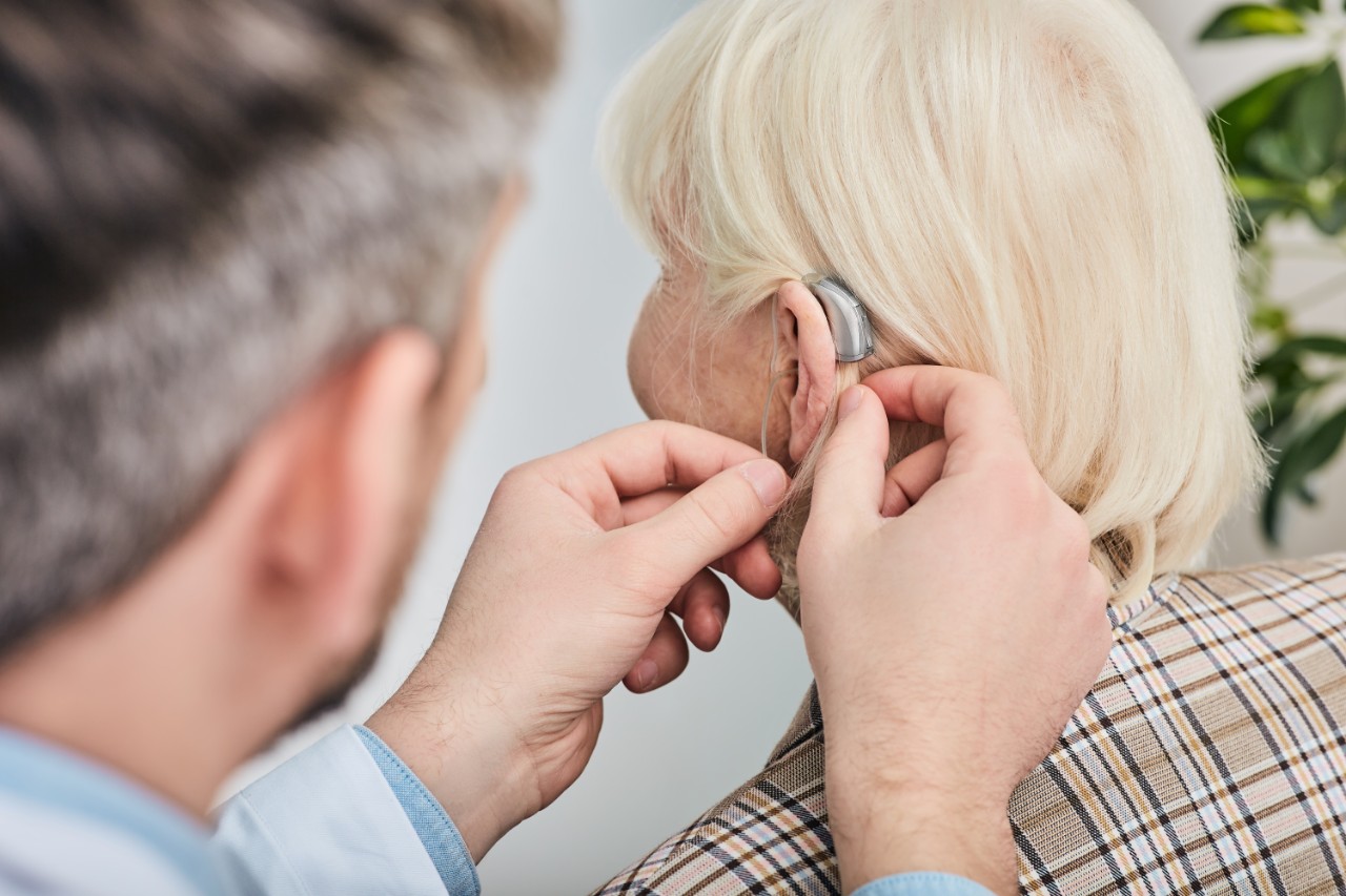 Médecin plaçant un appareil auditif derrière l'oreille du patient