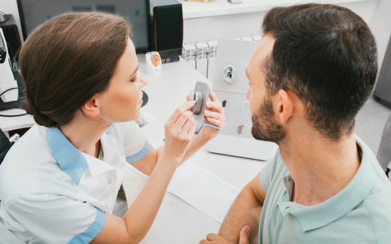 Médico mostrando a un paciente la funcionalidad del audífono