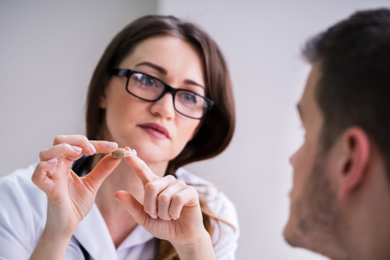 Fingers pointing at the specific part of the hearing aid fitted on the patient