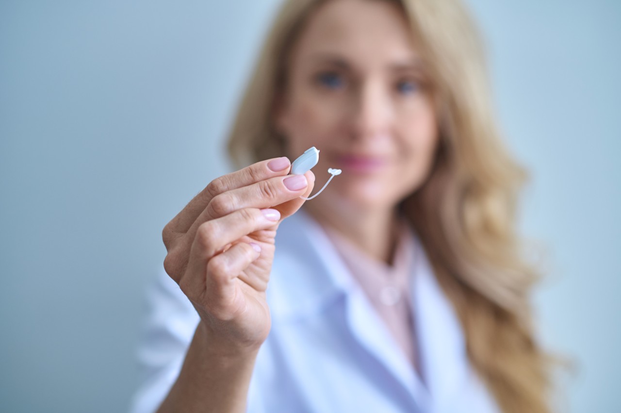 Woman doctor holding a zoomed-in hearing aid focused on the product