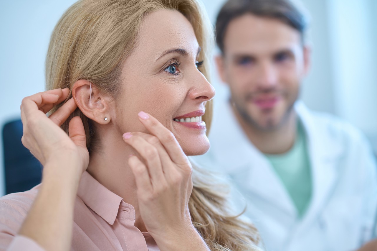 A blond woman wearing a hearing aid in front of a doctor