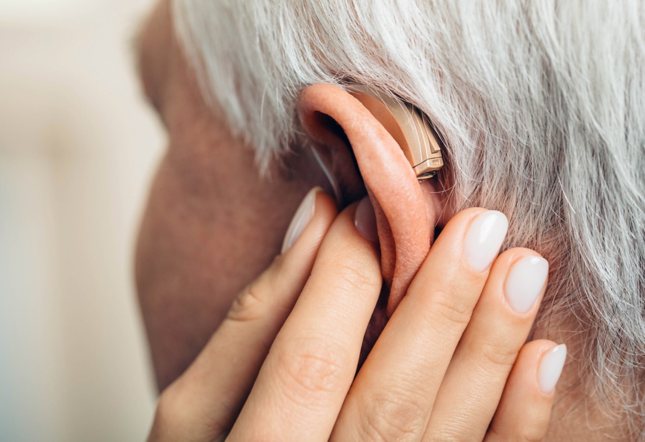 Elderly woman placing her hand on the hearing aids, showing the back part of the device