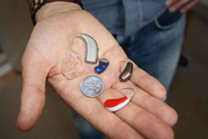 A hand with hearing aids and small objects to demonstrate how little they are